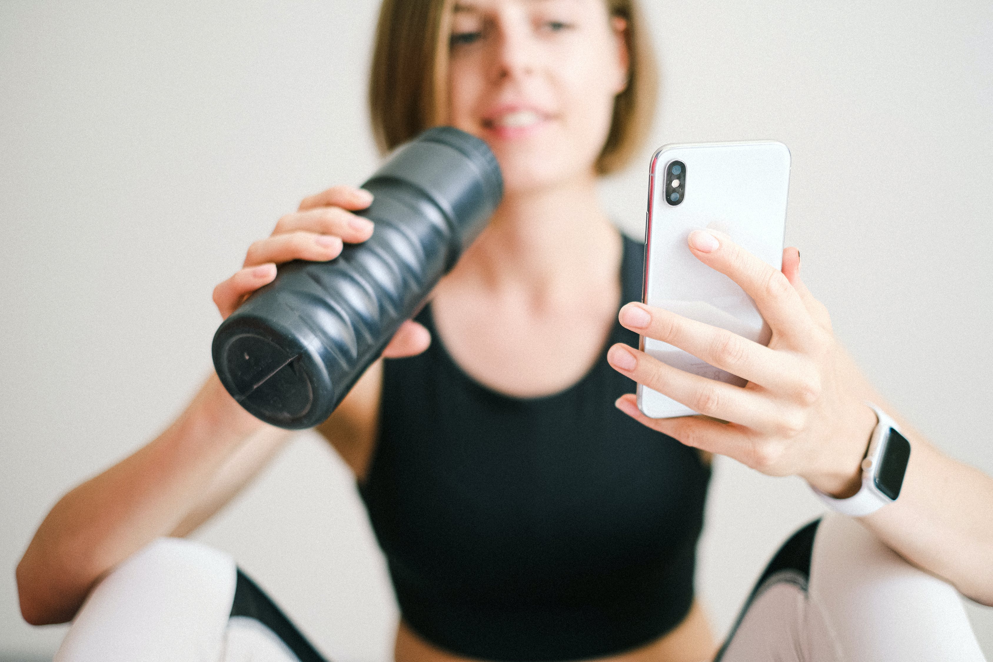 mulher com roupa de academia, segurando uma garrafa de água e olhando o celular